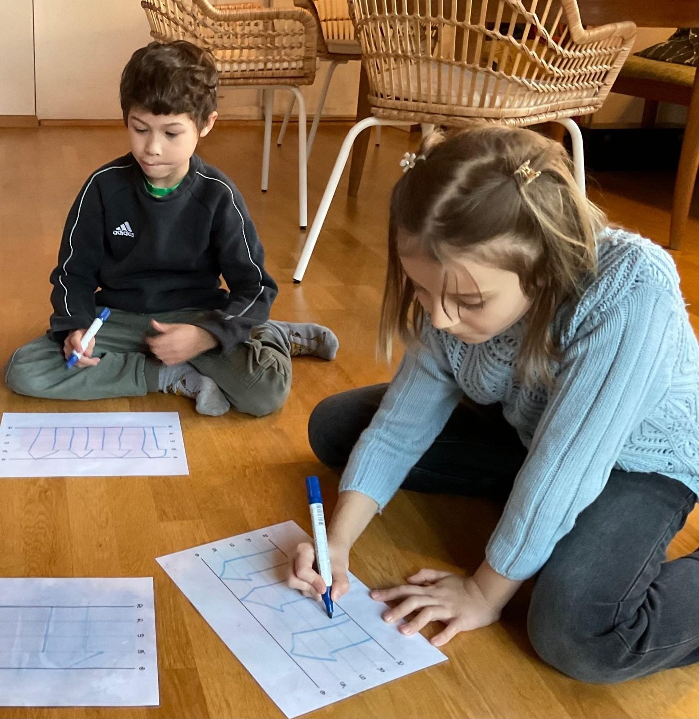Two children practising Thai writing exercises on worksheets
